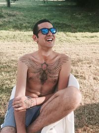 Shirtless man wearing sunglasses sitting on chair in park