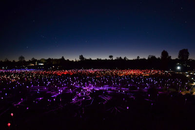 Crowd on illuminated field against clear blue sky at night