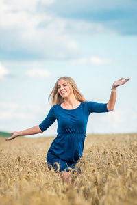 Smiling young woman standing on field against sky