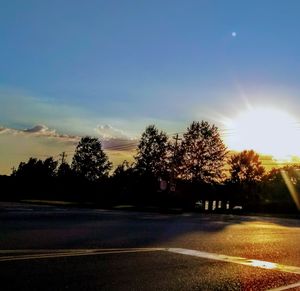 Silhouette trees by road against sky during sunset