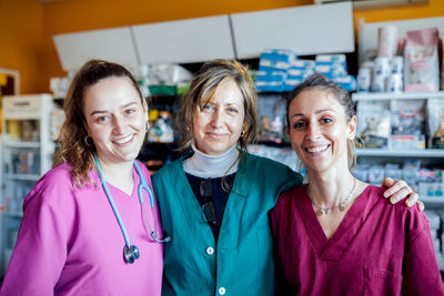 Group of positive female veterinarians in uniforms looking at camera while standing in veterinary clinic with medical supplies during work