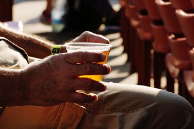 Midsection of man holding alcohol while sitting outdoors