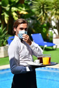 Portrait of waiter holding juice against plants