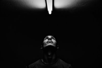 Young man looking towards fluorescent light on ceiling in darkroom