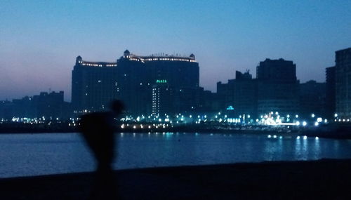 Silhouette buildings by river against clear sky at night