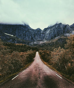 Empty road leading towards mountains against sky