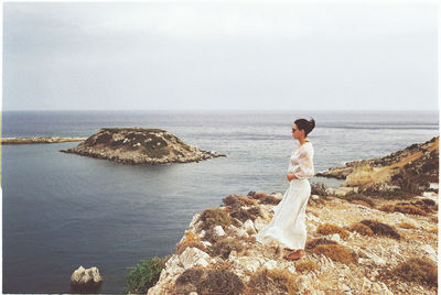 Side view of woman looking at sea while standing on rock against clear sky