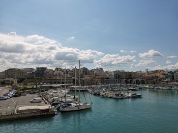 Sailboats moored in harbor by buildings against sky