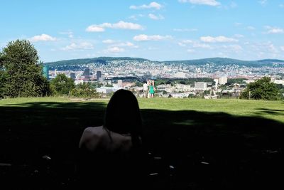 Rear view of man sitting on cityscape against sky