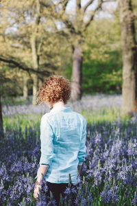 Woman standing amidst purple flowering plants at forest