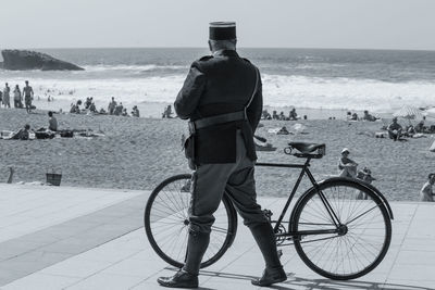 Rear view of security guard with bicycle walking by beach