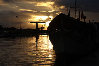 Silhouette built structure by river against sky at sunset