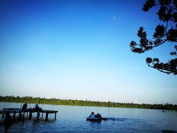 Silhouette people on riverbank against clear blue sky