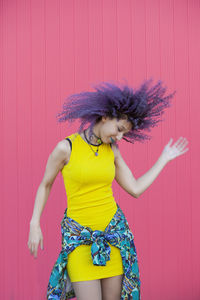 Woman tossing hair while standing by pink wall