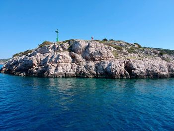 Rock formations by sea against clear blue sky