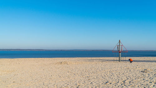 Boy by structure at beach against clear blue sky