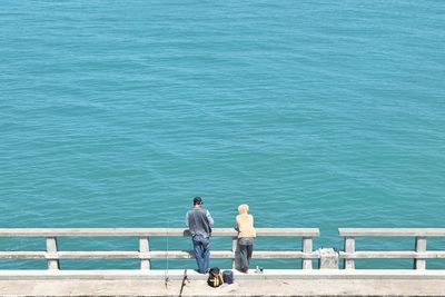 Rear view of people fishing while standing on pier by sea