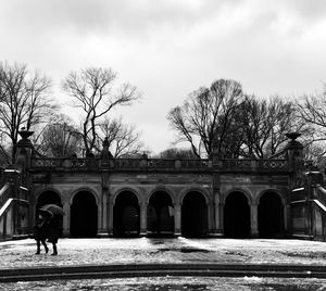 People walking by bare trees and building against sky