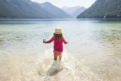 Rear view of toddler girl running into chilliwack lake, b.c., canada.