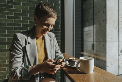 Mid adult woman text messaging on smart phone while sitting in cafe