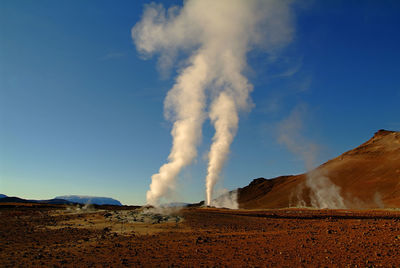 Smoke emitting from volcanic mountain against clear blue sky