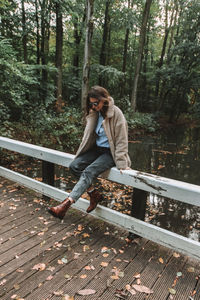 Full length of young man sitting on railing in forest