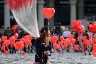 Woman holding red balloons with umbrella standing in city