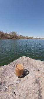 Coffee cup by lake against clear sky