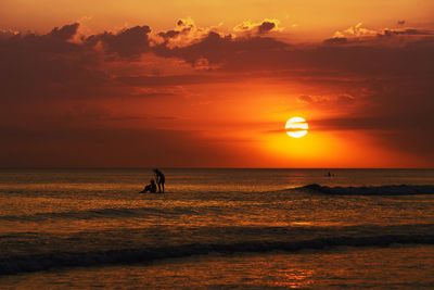 Silhouette people on sea against sky during sunset