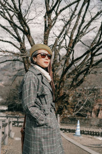 Portrait of young woman standing by bare tree