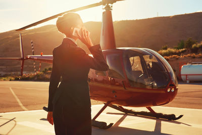Businesswoman talking on mobile phone while standing by helicopter during sunny day