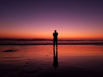 Rear view silhouette man standing at beach against sky during sunset