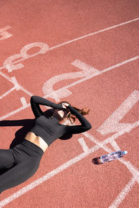 High angle view of tired woman lying with water bottle on running track