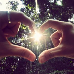 Close-up of hands making heart shape against bright sun