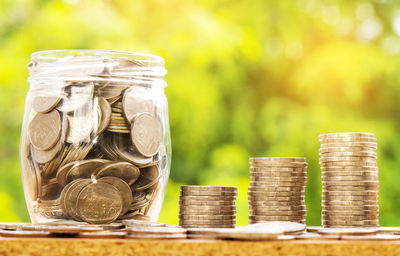 Close-up of coins stack by jar on table