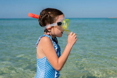 Child in blue swimsuit with snorkeling mask standing on sandy beach. girl is ready for diving