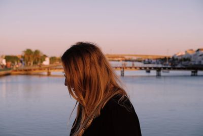 Side view of woman standing against river during sunset