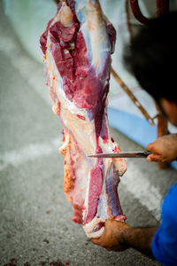 A man with a knife is cuttting the meat hanging on the hook.