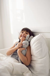 Child boy lies in a white children's bed with a blanket in a room with toys rabbits hug