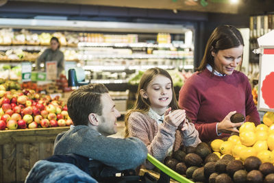 Side view of smiling father looking at daughter and woman shopping in supermarket