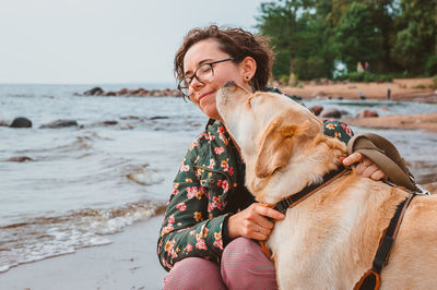 A dog kisses a girl on the cheek against the background of the sea. walk with a fawn labrador