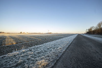 Road amidst field against clear sky