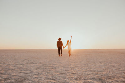 Rear view of woman walking at beach against clear sky