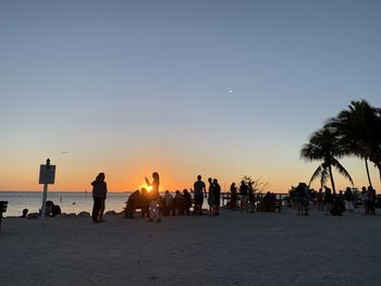 People on beach against clear sky during sunset