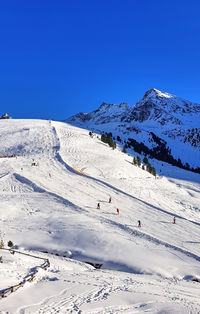 Scenic view of snowcapped mountains against sky, people skiing.