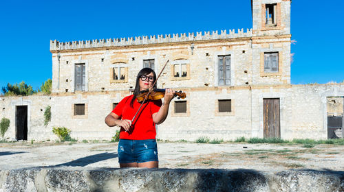 Mid adult woman playing violin while standing against building