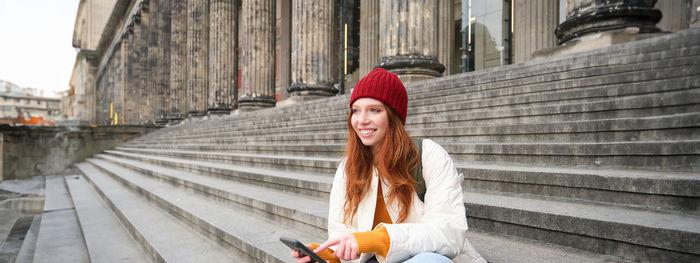 Portrait of young woman standing against building