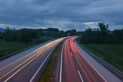 Light trails of vehicles on street against cloudy sky