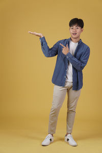 Portrait of young man standing against yellow background