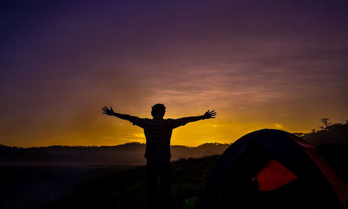 Silhouette man standing by built structure against sky during sunset